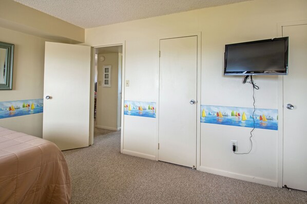 A hotel room with a bed, a television mounted on the wall, and doors with nautical-themed artwork.