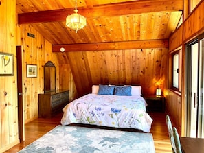 Quarto acolhedor de cabana de madeira, com uma cama grande, penteadeira, espelho e lustre.