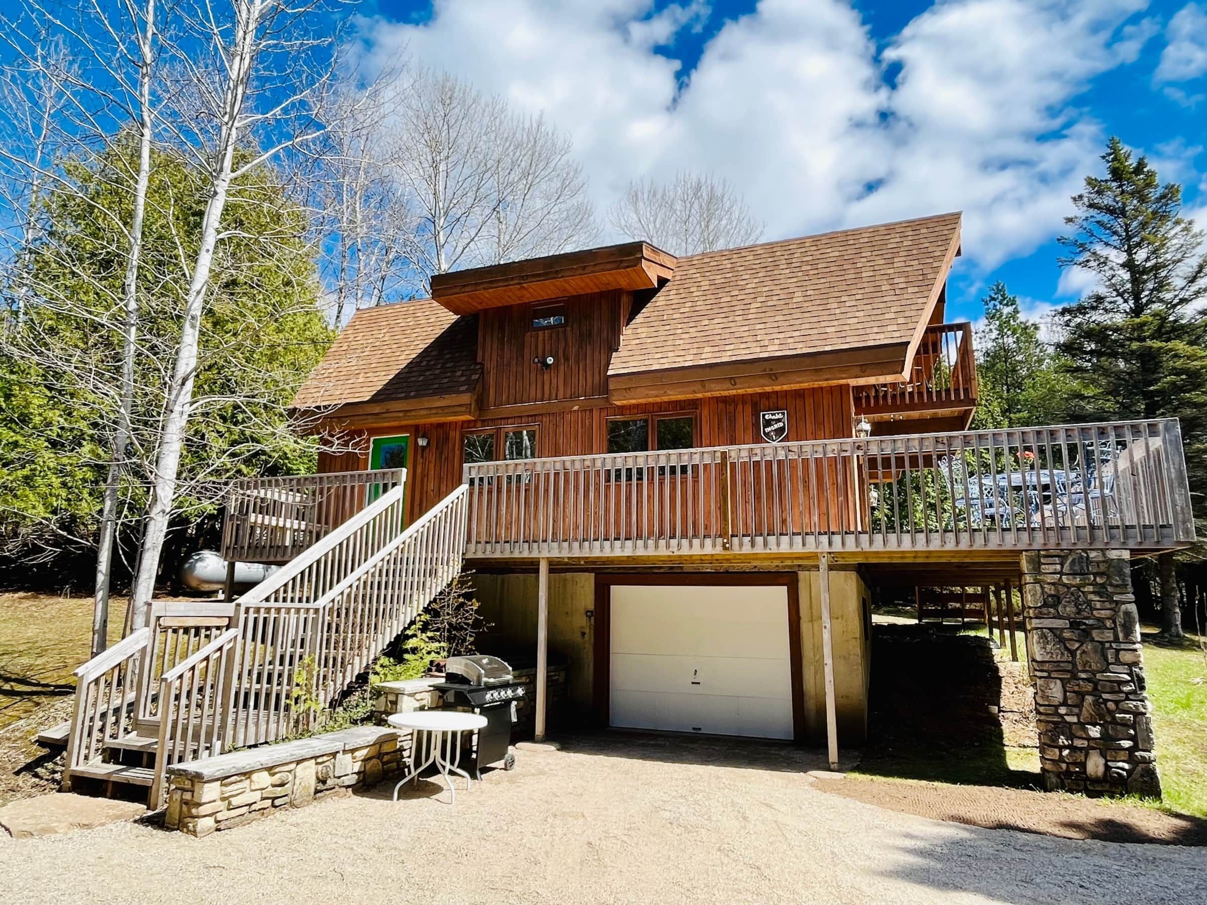 Eine zweistöckige Holzhütte mit Balkon, Garage und Sitzgelegenheit im Freien.