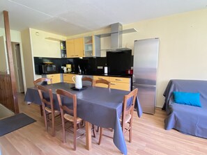 A compact kitchen with a dining table, chairs, a refrigerator, and a sofa. - La Mongie - Apt 2 ch - Parking Couvert - 46m² - 8 Pers (Bagnères-de-Bigorre)