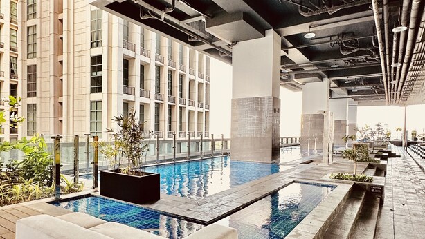 Espaço moderno de piscina interna com uma piscina retangular, assentos acolchoados brancos e vista para um edifício alto.
