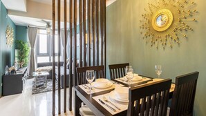 Uma área de refeições com uma mesa posta para dois, um relógio decorativo na parede e vista para outro cômodo.