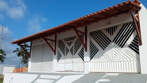 A building with a red-tiled roof, white walls, and large windows with white grills. - Casa na Praia do Atalaia em Salinas (Salinópolis)