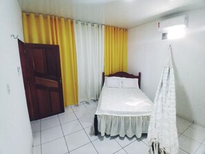 A small, clean room with a bed, curtains, a door, and a wall-mounted air conditioner. - Casa na Praia do Atalaia em Salinas (Salinópolis)