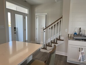 A kitchen with a marble countertop, wooden staircase, and white cabinetry.