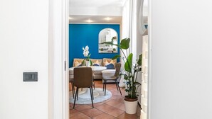 A modern living room with a blue accent wall, a dining area with a round table and chairs, and a large potted plant.