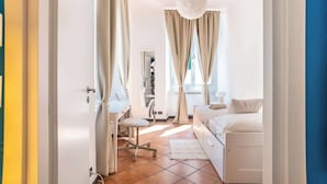 A bedroom with a bed, a desk, and a chair, with curtains and a hanging light fixture.