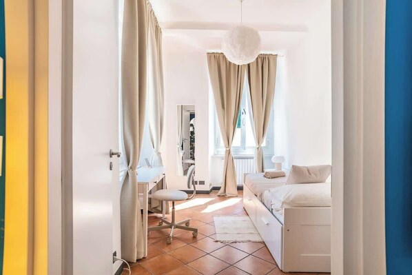 A bedroom with a bed, a desk, and a chair, with curtains and a hanging light fixture.