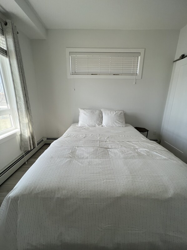 Une chambre avec un grand lit, une fenêtre avec des stores et un radiateur.