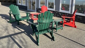 An outdoor seating area with green and red Adirondack chairs and tables in front of a building with large windows. - Luxury Airport Suite 2Bed 2Bath w/ heated parking (Calgary)