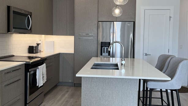 A modern kitchen with a central island, stainless steel appliances, and pendant lighting. - Luxury Airport Suite 2Bed 2Bath w/ heated parking (Calgary)