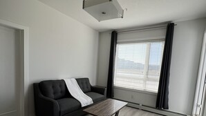 A modern living room with a dark grey sofa, a wooden coffee table, and a large window with blinds. - Luxury Airport Suite 2Bed 2Bath w/ heated parking (Calgary)
