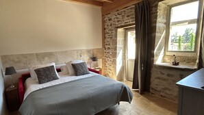 Un dormitorio con cama, mesita de noche, lámpara, ventana con cortinas y vistas al exterior.