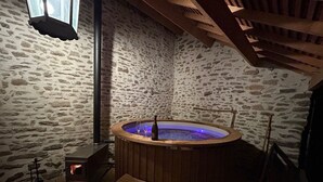 Una habitación de paredes de piedra con un tinaco de hidromasaje de madera, un banco y una chimenea.