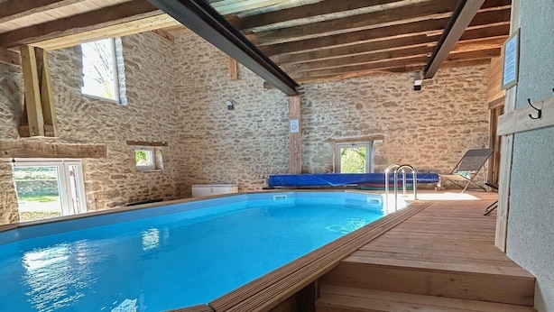 Una piscina con escalones de madera que llevan hasta ella, rodeada de muros de piedra y vigas de madera.