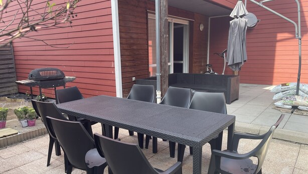 En udend ørs patio med et bord, stole, grill og et overdækket område med en stol.