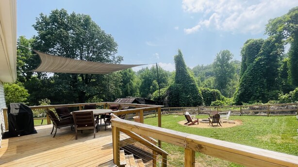 En træterrasse med udendørs møbler, grill og en græsplæne med træer.