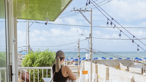 Un balcón con vista a la playa, una barandilla y una planta en maceta.