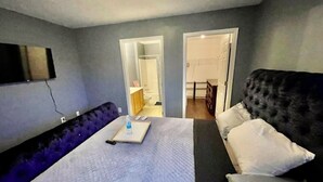 Een hotelkamer met een bed, een bank, een aan de muur bevestigde televisie en een badkamer door een open deur zichtbaar.