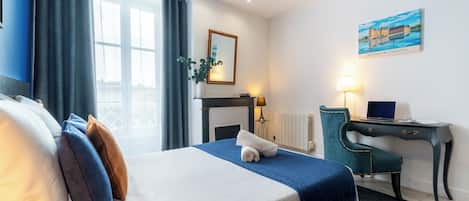 Ein Hotelzimmer mit Bett, Schreibtisch, Stuhl, Lampe, einem Gemälde und einem Fenster mit Vorhängen.
