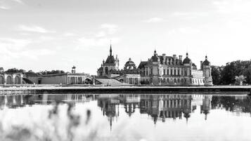 Un bâtiment historique doté d’un grand dôme central et d’un dôme plus petit situé à gauche, dont le reflet se mire dans une étendue d’eau calme.