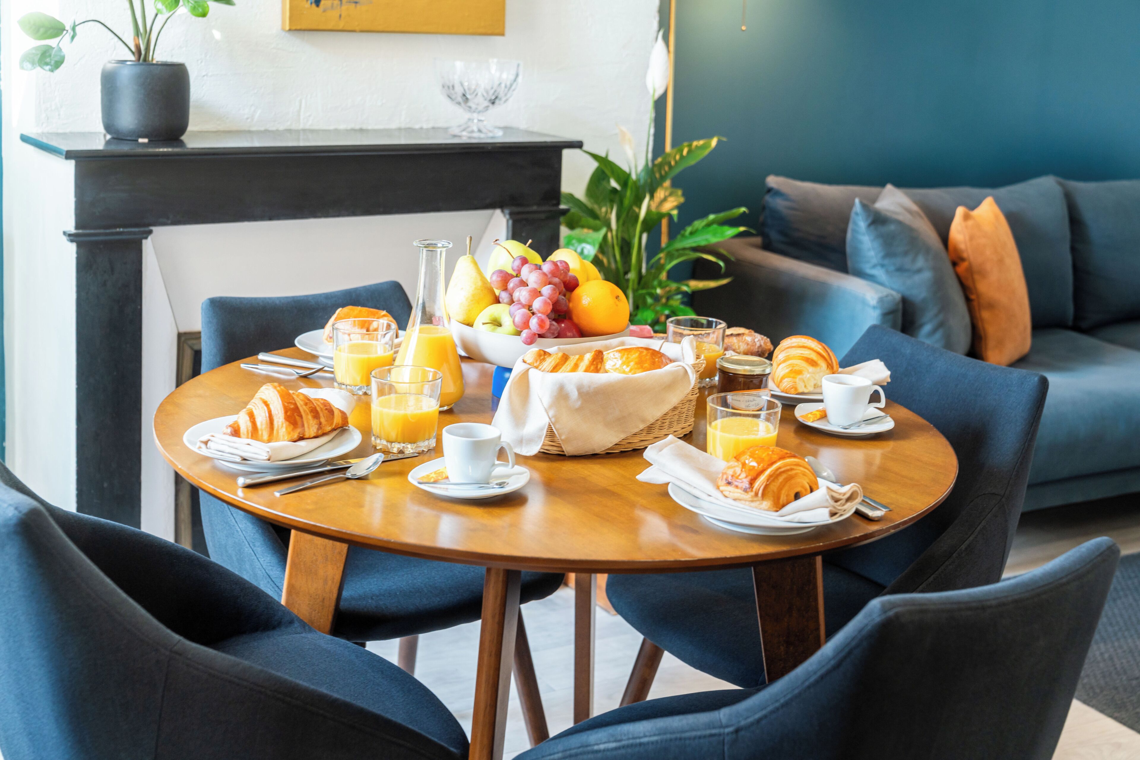 A breakfast setting with a round wooden table, chairs, and a variety of food and drinks.