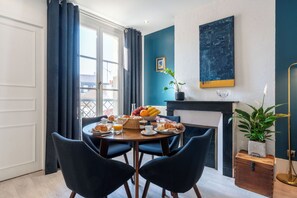 Comedor con mesa redonda, sillas, alimentos para el desayuno y vistas a través de una ventana.