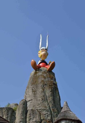 A statue of a character with horns and a red outfit sitting on a rock formation. - Le Logis Cantilen (LAMORLAYE)