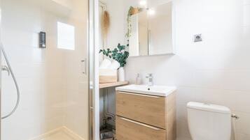 Een moderne badkamer met een douchecabine van glas, een houten wastafelmeubel met een wastafel en een toilet.