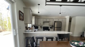 Una cocina moderna con armarios blancos, una isla central y un comedor con mesa y sillas de madera.