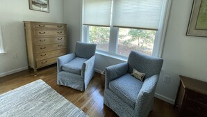 Una habitación con dos sillones, un aparador de madera y una ventana con persianas.