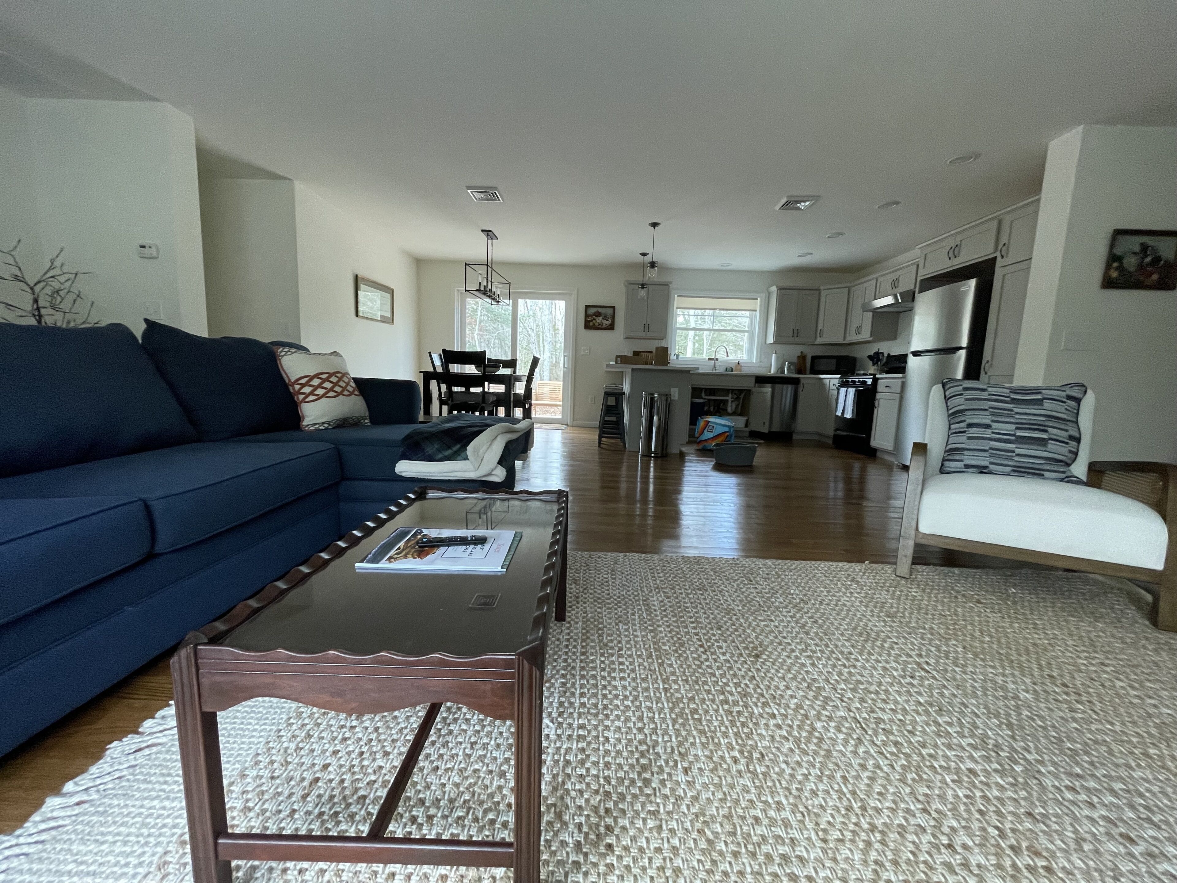 A spacious living room with a blue sofa, a coffee table, and a view into the kitchen area.