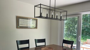 Un comedor con una mesa de madera, sillas negras, un certificado enmarcado en la pared y vista a zonas verdes a través de un ventanal.
