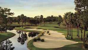 A golf course with sand bunkers, a pond, and palm trees.