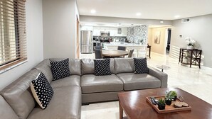 A modern living room with a grey sectional sofa, a wooden coffee table, and a kitchen in the background.