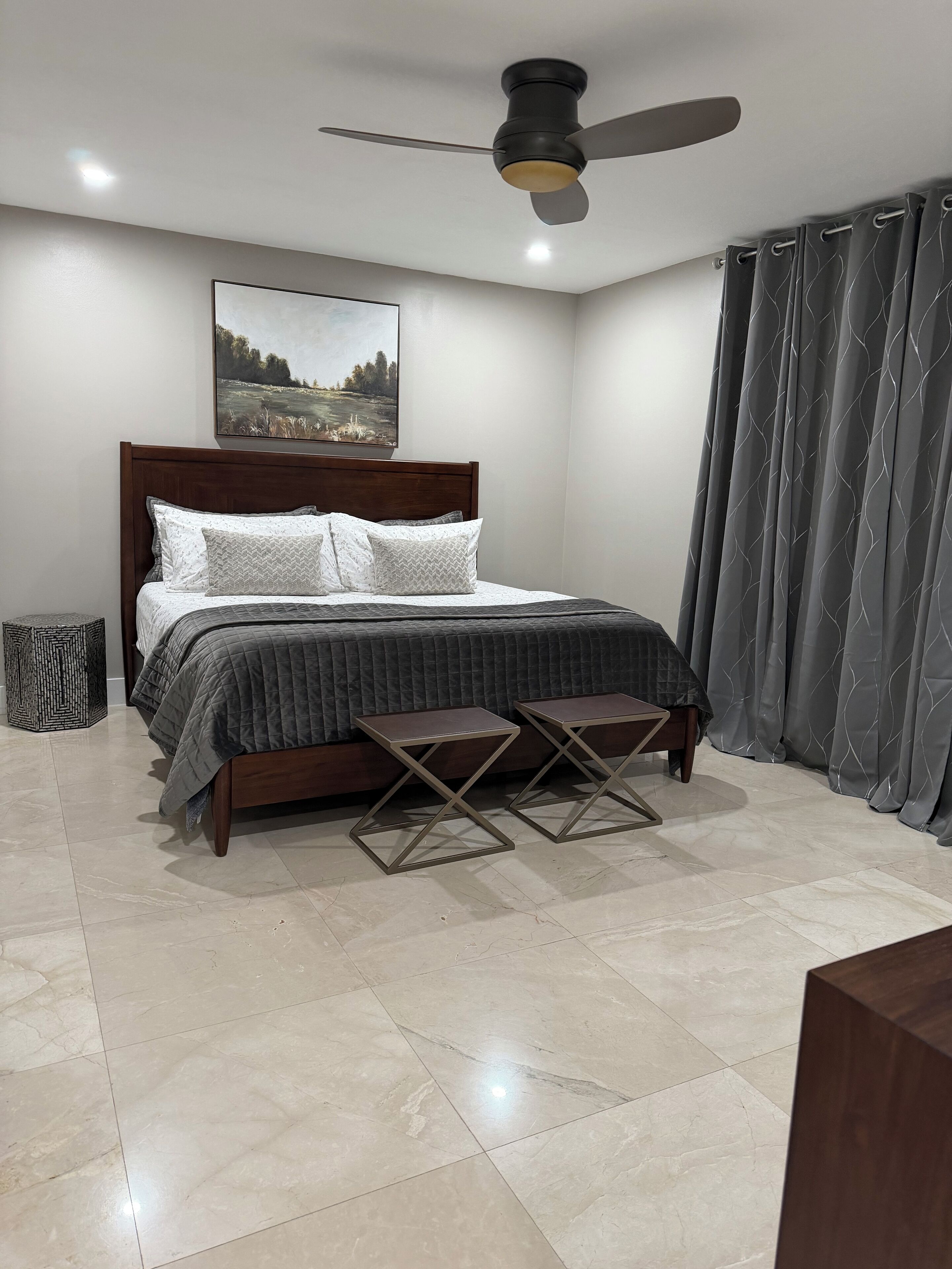 A bedroom with a bed, two nightstands, a ceiling fan, and a painting on the wall.