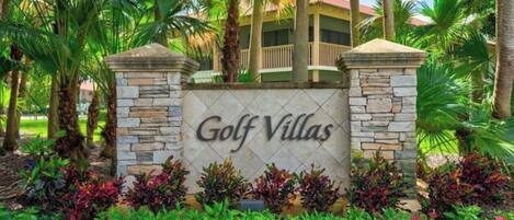 Letrero para Golf Villas, con muro de piedra y jardines tropicales.