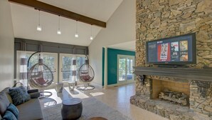 Una sala de estar moderna con chimenea de piedra, un televisor de pantalla plana grande y un rincón de descanso acogedor con un sofá y dos sillones colgantes.