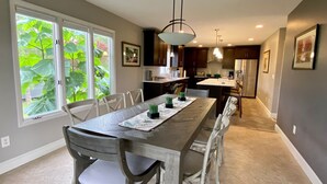 Una cocina amplia con una larga mesa de comedor, electrodomésticos modernos y ventanas grandes con vistas al verdor.