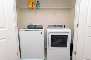 A laundry room with two stacked washers and dryers, a shelf with cleaning supplies, and a door leading to another room. - Luxury Townhome WestOC -4 BRS / golf / asssateague (Berlin)