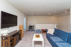 A living room with a flat-screen TV, a blue sofa, a wooden coffee table, and a small white table. - Luxury Townhome WestOC -4 BRS / golf / asssateague (Berlin)