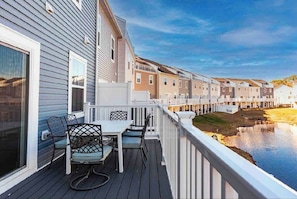 A deck with outdoor furniture overlooking a water body and a row of townhouses. - Luxury Townhome WestOC -4 BRS / golf / asssateague (Berlin)