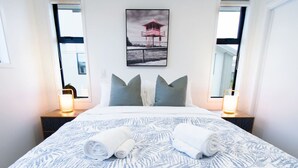 Une chambre d’hôtel avec un grand lit, deux tables de chevet avec des lampes, un tableau encadré au mur et une fenêtre donnant sur un beau paysage.