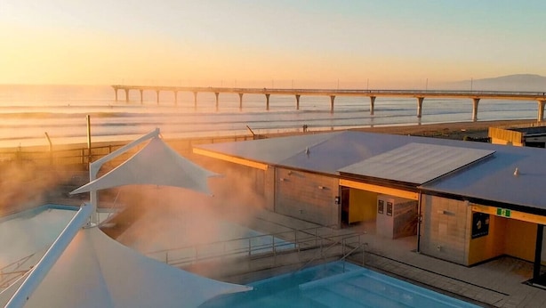 Un espace piscine aménagé sur le toit, offrant une vue sur un pont enjambant une étendue d’eau.
