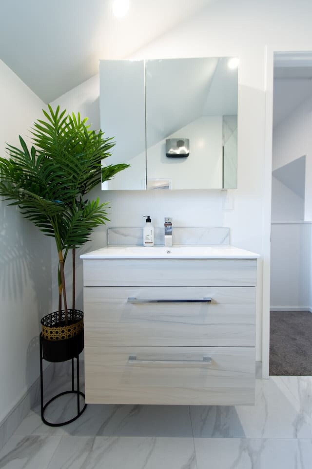 Een moderne badkamer met een wit wastafelmeubel, een grote spiegel en een kamerplant.