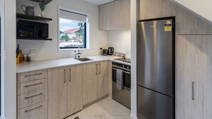 A modern kitchen with light wood cabinets, a stainless steel refrigerator, a window with a view of the outside, and a microwave on a shelf. - Explore Addington and CBD 1 Bed w/Carpark (Christchurch)