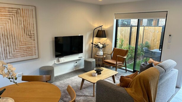 A modern living room with a flat-screen TV, a sofa, a coffee table, and a dining area with a table and chairs.