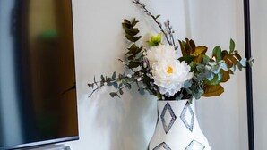 A living room with a TV, a decorative vase with flowers, a bowl of coffee beans, and a small table.