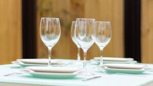 Une table dressée à l’extérieur, avec trois verres à vin, des assiettes et des couverts.
