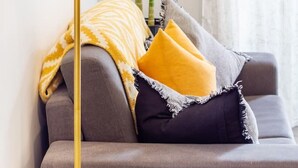 Un salon moderne avec un canapé gris, des coussins jaunes et noirs, un plaid jaune et un grand lampadaire.